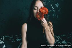 Studio portrait of woman holding gerbera flowers against dark floral background 4BrJk4