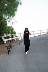 Woman in dark athletic outfit walking dog on a leash in the street