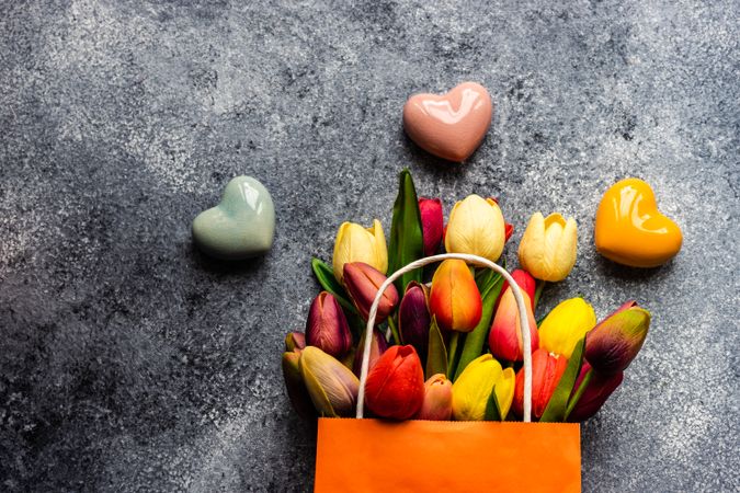 Thee colorful ceramic heart ornaments on grey counter with bag of fresh tulips
