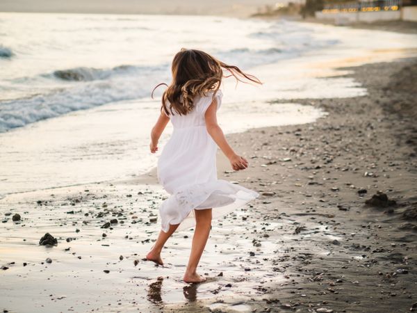 Adorable girl walking and playing on seaside at sunset