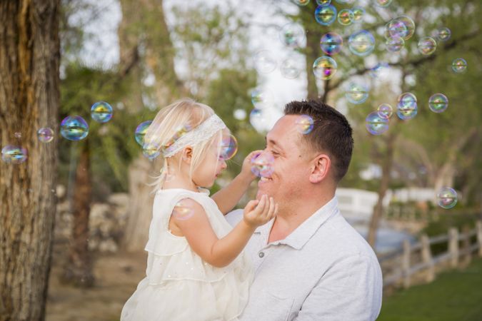 Father Holding Baby Girl Enjoying Bubbles Outside at Park