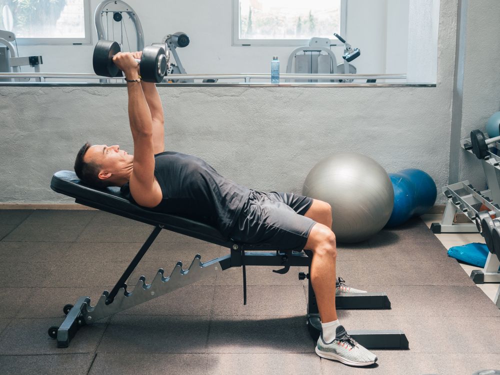 Strong man exercising with dumbbells on bench
