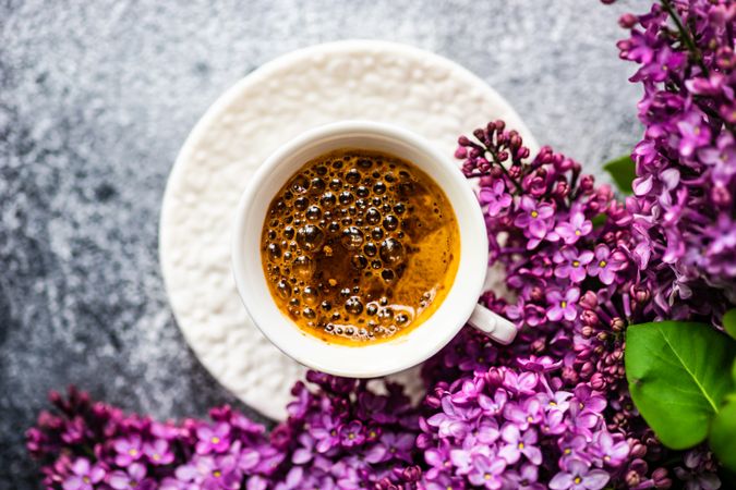 Top view of pink lilac flowers surrounding cup of espresso