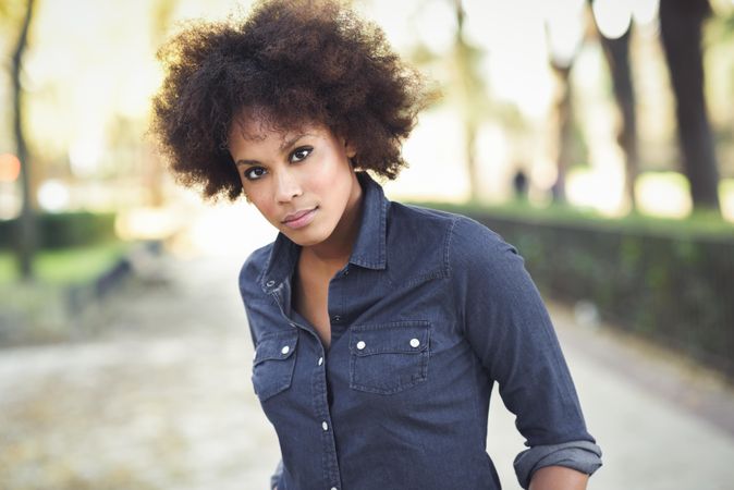 Serious woman standing outside in denim shirt looking at camera, copy space