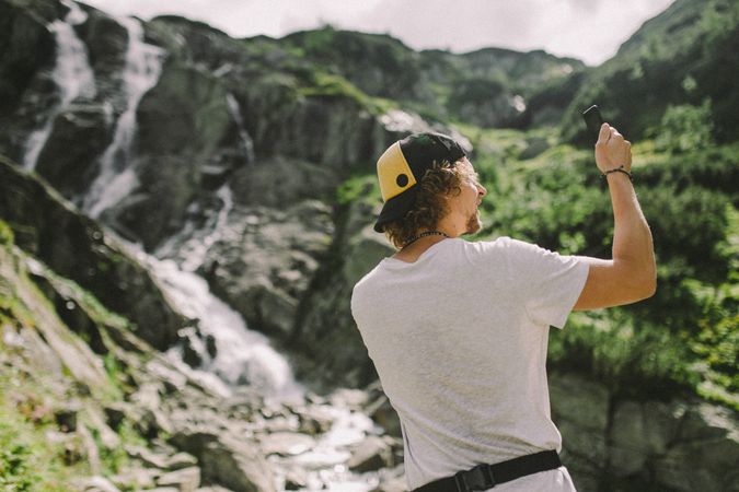 Back view of blonde man holding a phone standing near mountains