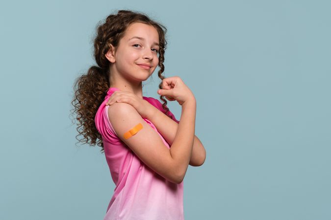 Girl flexing arm with orange bandage after receiving vaccine shot