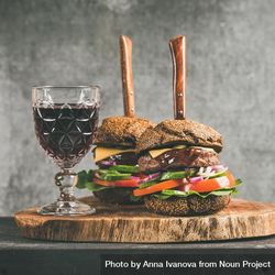 Two cheeseburgers, stacked with fresh vegetables, on wooden board, with wine, knifes, square crop 4M6w1b