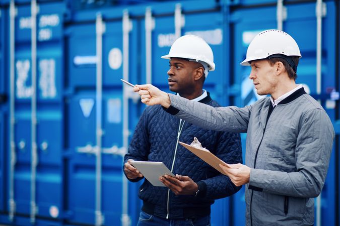 Two men in hard hats pointing towards a building project