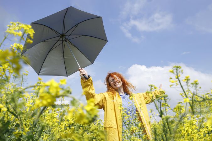 Joyful red haired woman dancing in a yellow field holding umbrella