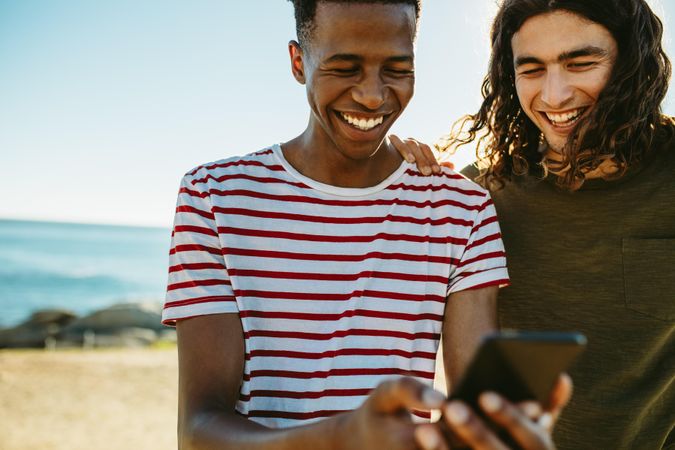 Two young friends outdoors looking at mobile phone and smiling