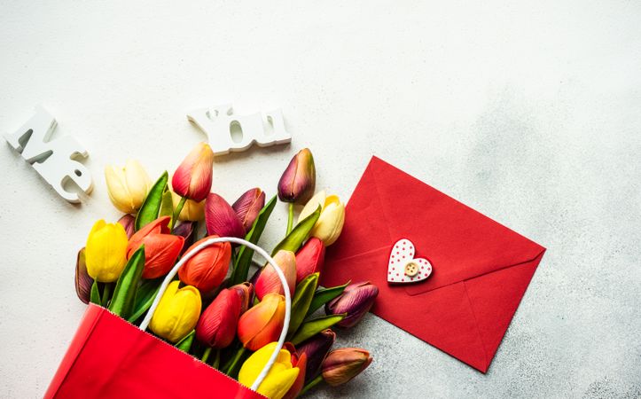 Tulips in shopping bag with present and red envelope on grey counter