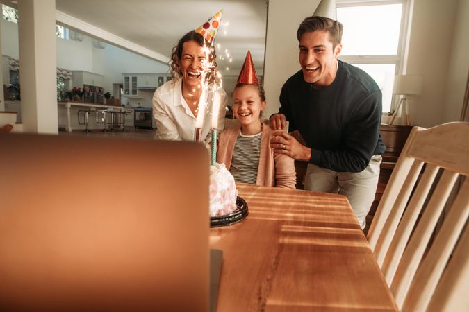 Family wearing party hats with birthday cake on table and looking at laptop