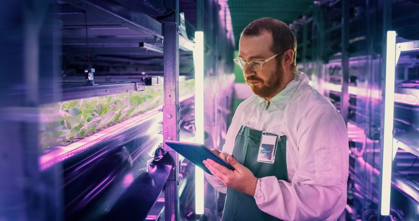 Close Up Portrait of a Farming Technician Standing Next to a Row of Fresh Crops Growing at a Modern Vertical Farm.