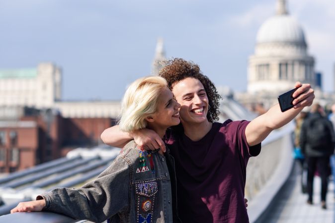 Blonde female and curly haired boyfriend taking picture on bridge in London