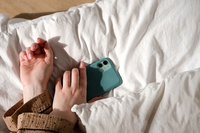 Hand holding smartphone on bed