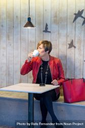 Woman in red coat sitting in cafe sipping coffee bGpel0