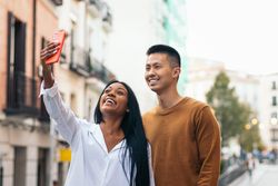 Asian man and Black Latina woman taking a selfie with smartphone