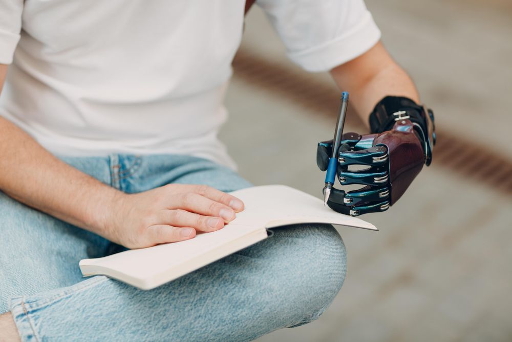 Cropped image of person with prosthetic hand writing on a notebook