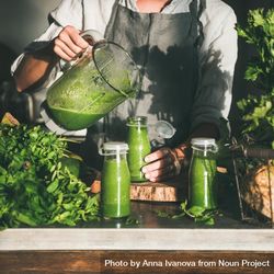 Woman Pouring Green Smoothie Into Jars In Kitchen, Square Crop - Free ...