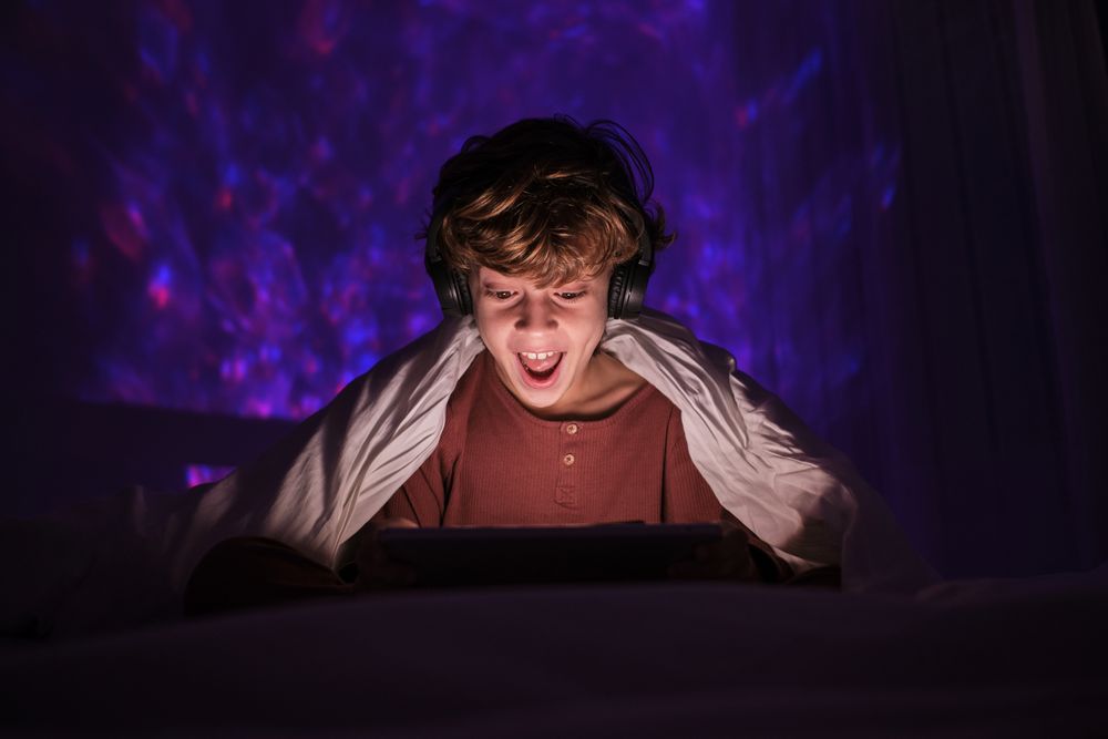Amazed boy browsing tablet in darkness at home