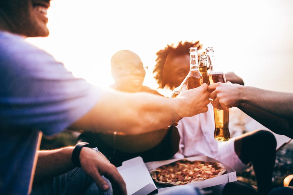 Group of friends toasting over beers, and pizza at sunset