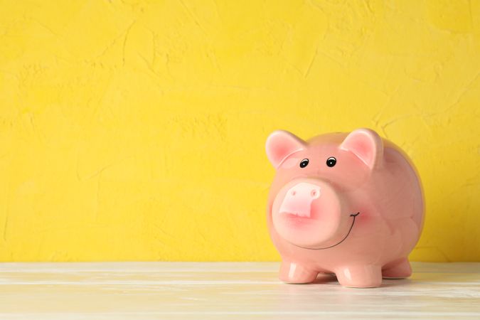Happy piggy bank on wooden table against color background, space for text. Finance, saving money