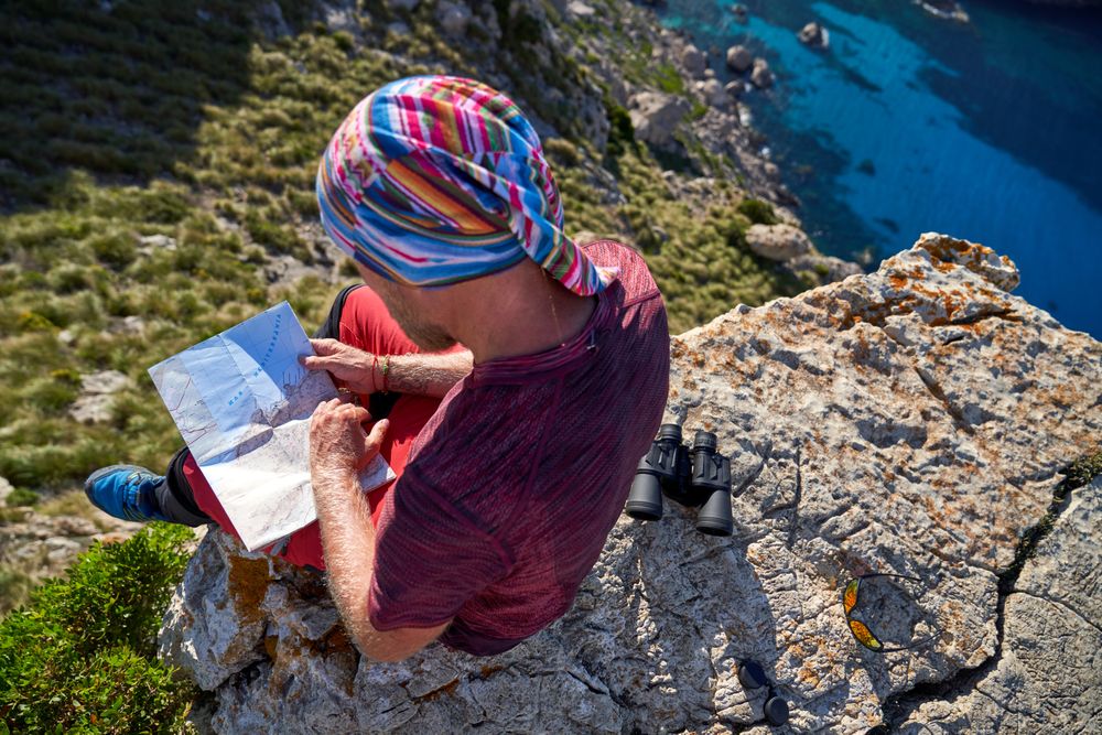 Unrecognizable hiker reading map on cliff