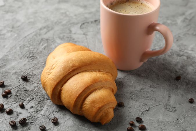 Croissant and pink mug of coffee on grey table