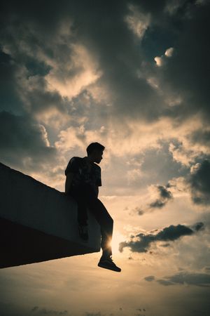 Silhouette of a man sitting on the edge of rooftop at sunset