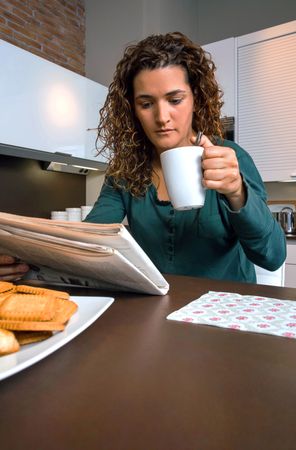 Woman reading morning papers at breakfast with cup of coffee