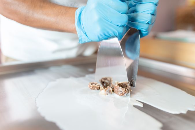 A worker is using spatulas to chop chocolate and mix it with milk on a rolled ice cream machine