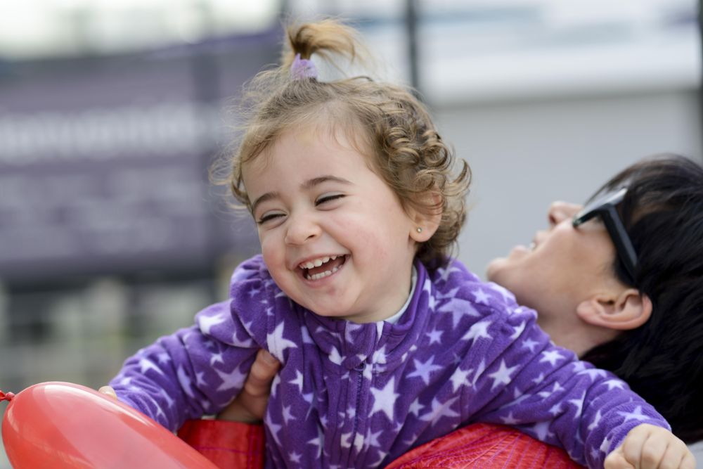 Little girl smiling and laughing in her mother’s arms