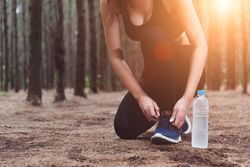 Woman sitting on forest floor tying shoes with sun flare