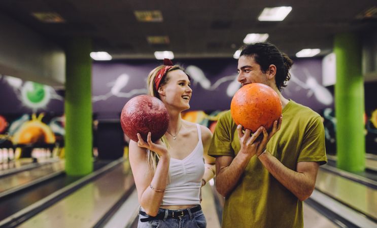 Cheerful young couple at the bowling alley with balls looking at each other