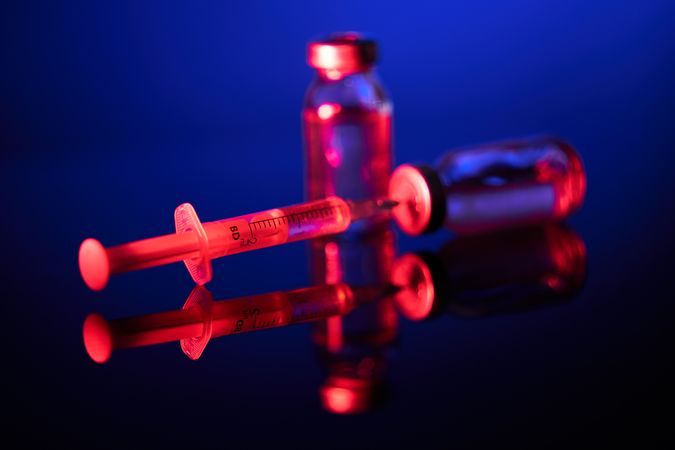 Syringe with needle inserted into vial in dark room