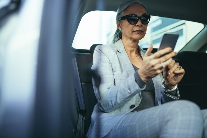 Older businesswoman traveling by a car using smart phone
