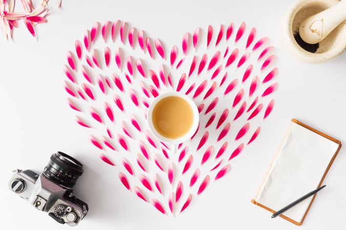 Heart made of pink flower petals with coffee, camera and stationary