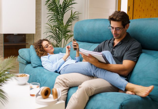 Chill couple resting on sofa while bonding and working in living room