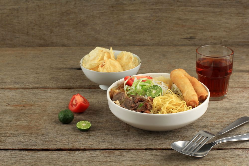 Dinner of Indonesian beef noodle soup with noodles, beef, spring roll, cabbage and tomato