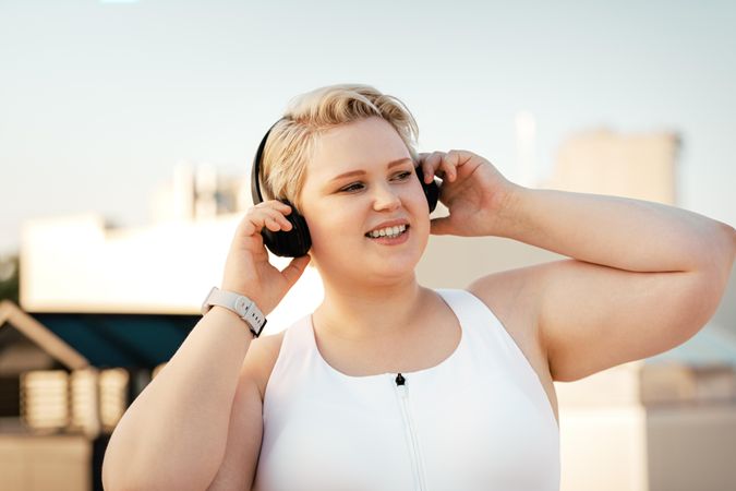 Blonde woman in exercise gear holding headphones to her ears outside
