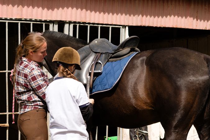 Instructor guiding young girl in saddling horse.