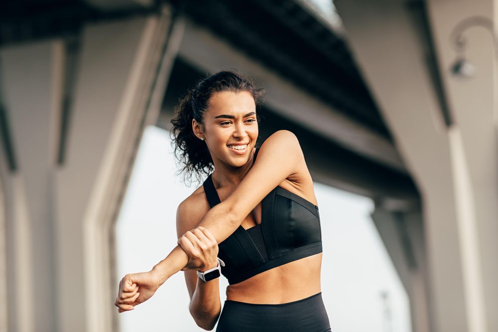 Smiling female stretching arm outdoors