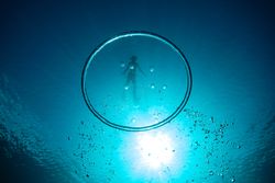 Bubble ring with diver swimming in blue water