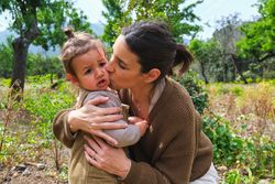 Young mother embracing and kissing daughter in lush park