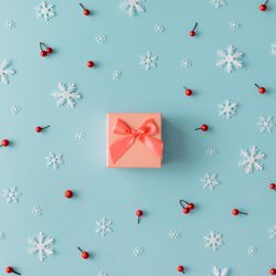 Christmas pattern made of snowflakes and red berries with orange present on blue background