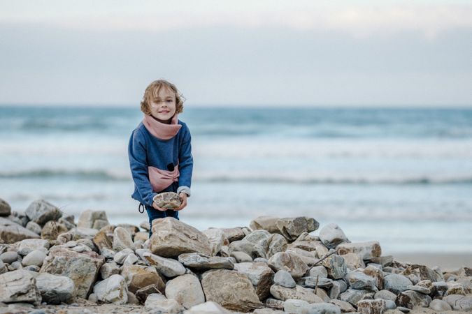 Smiling child near heap of stones on shore near water