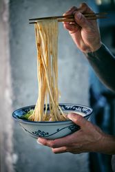 Crop man with noodles on chopsticks above tasty ramen