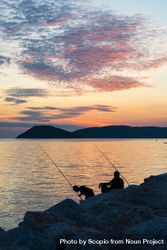 Silhouette of two fishermen sitting on rock near sea during sunset 0LpmR0
