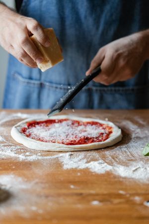 Crop cook grinding cheese on pizza
