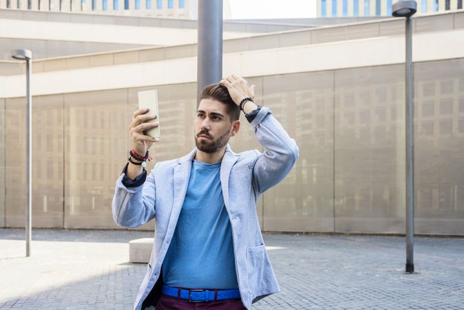 Man in blazer leaning on pole with hand on head taking a video call